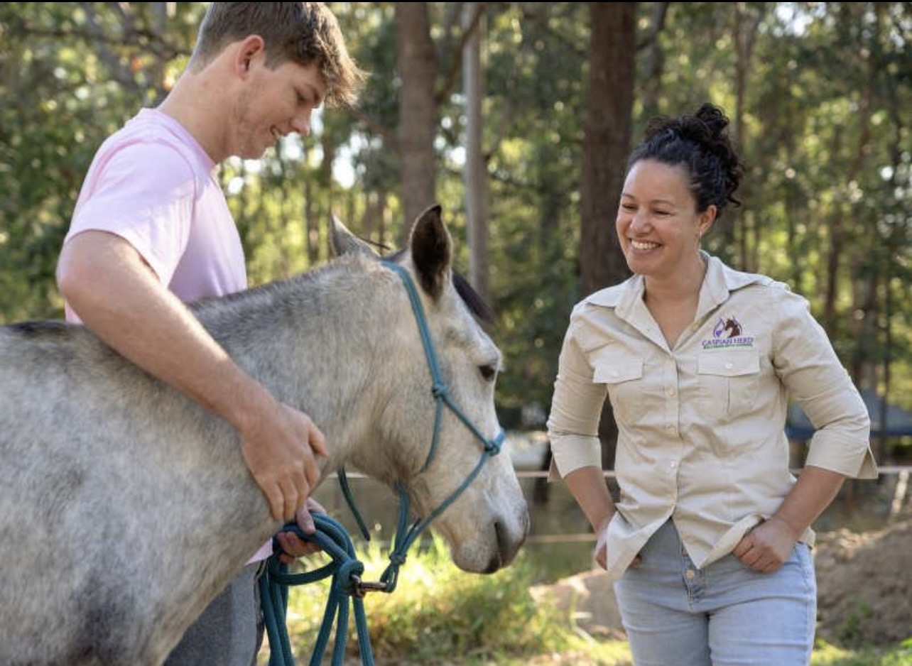 A consultant and a young man working together with a gray horse during a hands-on session